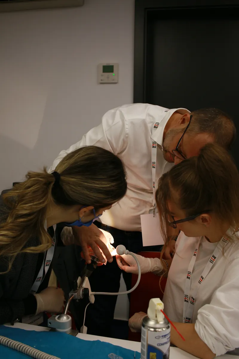 Dr. Cosmin Ulman se apleacă peste masa a două participante și le arată pe model